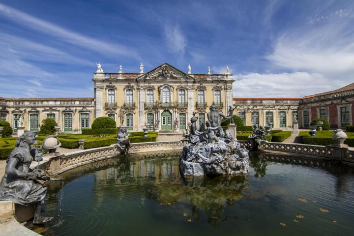 a castle surrounded by a body of water with Palace of Queluz in the background