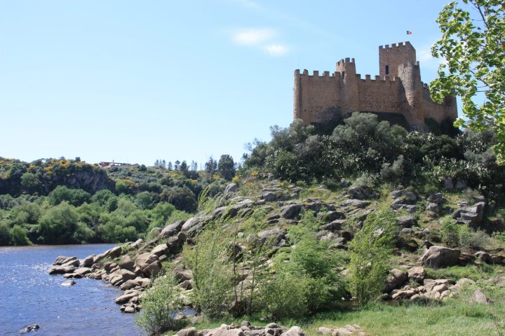 a castle on a rock next to a body of water with Castle of Almourol in the background