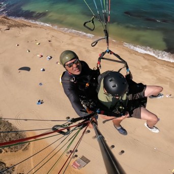 Two people paragliding over a beach with ocean in the background.