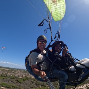 Two people paragliding over a landscape with clear blue sky and distant paraglider.