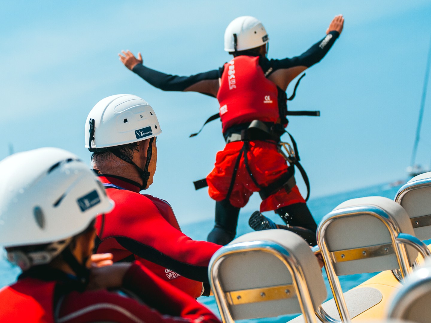 Person in red gear jumping off a boat, others watching, all wearing helmets.