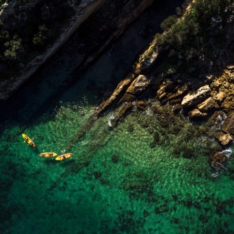 Aerial view of kayakers near a rocky shoreline and clear turquoise water.