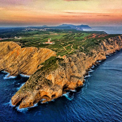 Aerial view of a rocky coastline with cliffs and a lighthouse at sunset.