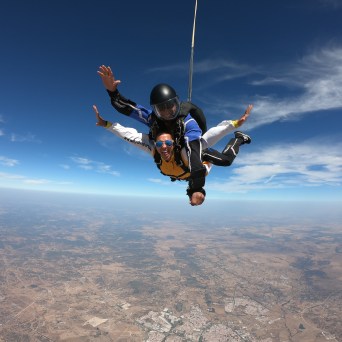Two people tandem skydiving with a view of the land and sky.