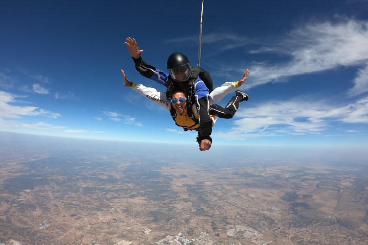 Two people tandem skydiving with a view of the land and sky.