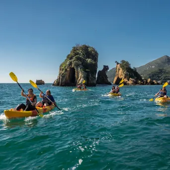 People kayaking in blue sea near rocky islands under clear sky.