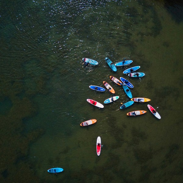 Aerial view of people on colorful paddleboards clustered on calm water.
