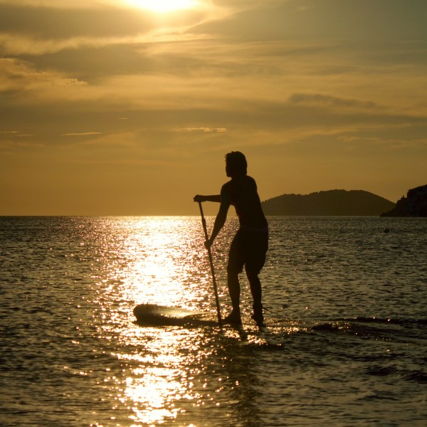 Silhouette of a person paddleboarding at sunset on calm water.
