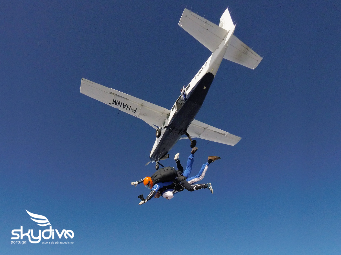 Two skydivers jumping from a small plane in clear blue sky.