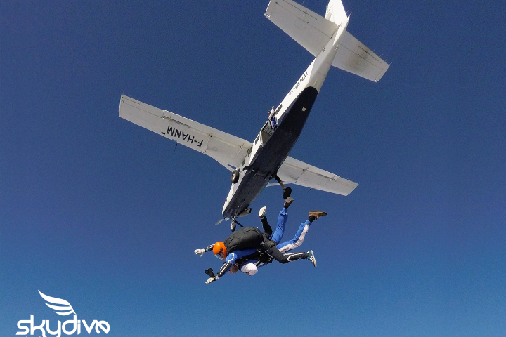 Two skydivers jumping from a small plane in clear blue sky.