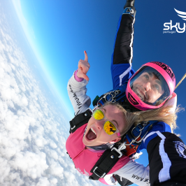 Tandem skydivers freefalling with excitement, blue sky, and clouds below.