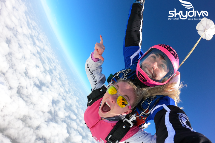 Tandem skydivers freefalling with excitement, blue sky, and clouds below.